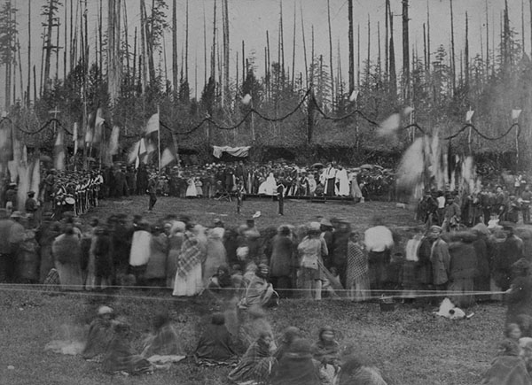 Group of Indigenous people stand in a circle surrounded by trees. Possibly the meeting between the Stó꞉lō and the B.C. Government.