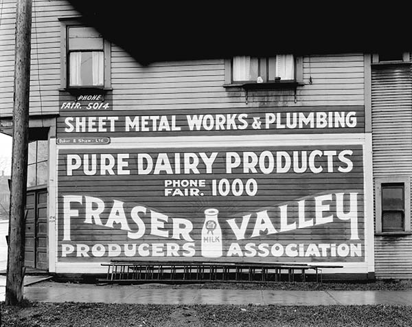 Billboard advertising the Fraser Valley Milk Producer's Association on the side of a wood-paneled building.