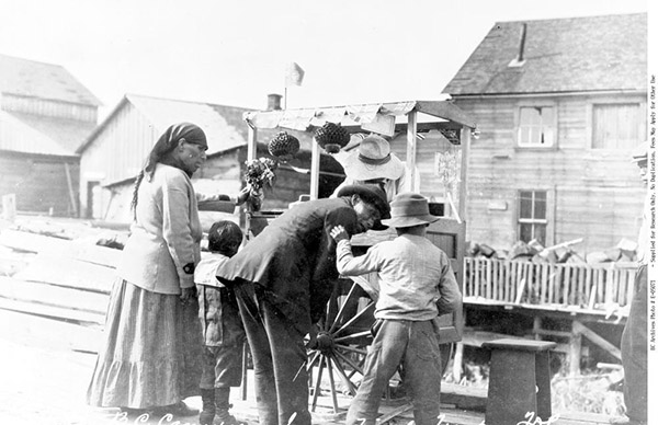 Indigenous woman, man, and two small children inspect wares for sale at a booth.