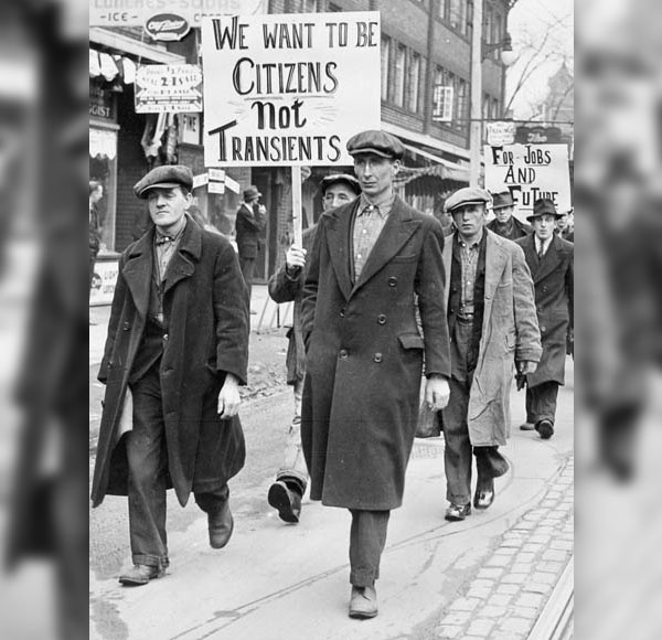 Group of men in caps and overcoats hold signs protesting unemployment.