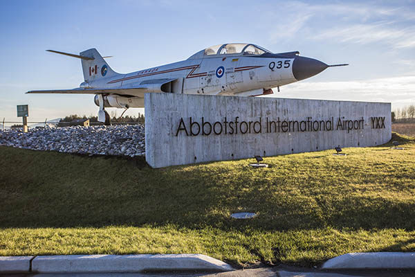 Welcome sign at the entrance of Abbotsford Airport positioned underneath a McDonnell F-101 Voodoo fighter jet with a maple leaf on it's side.