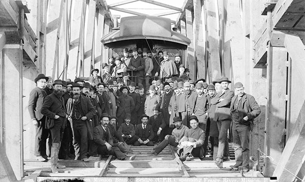 Group of men stand on a train that sits on a timber-framed bridge
