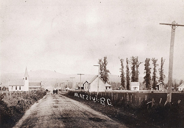 Dirt road with a distant horse and buggy with a church and farmhouses in the background.