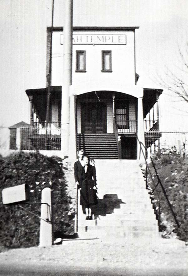 Man and woman stand on the steps leading up to a false-fronted building with a sign reading "Sikh Temple".