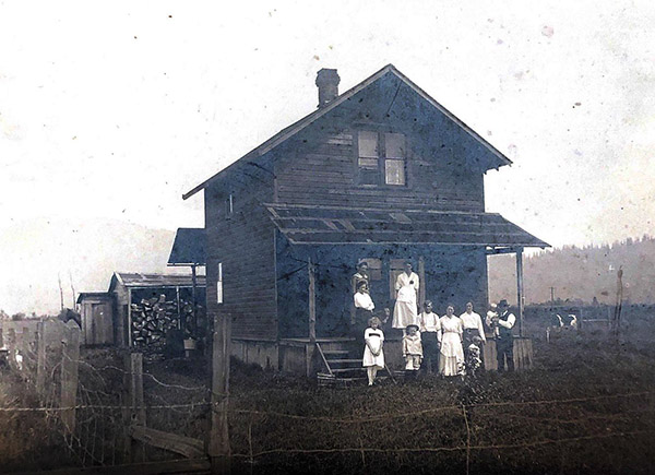 Family poses on the front porch of their simple timber-framed house.