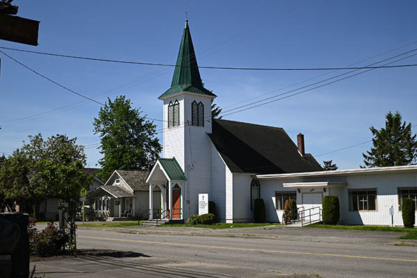 Old church with arched windows and a single steeple over the entrance and adjoining buildings.